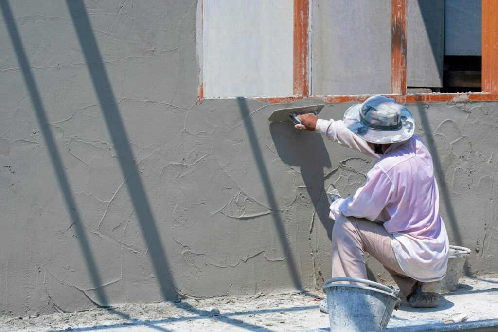 Side view of Asian builder worker plastering cement wall in house construction site