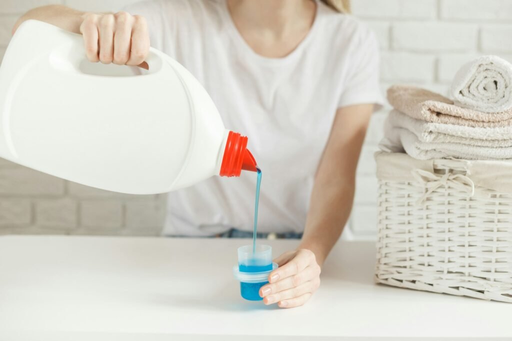 Woman pouring detergent into cap on table, close-up. Laundry concept