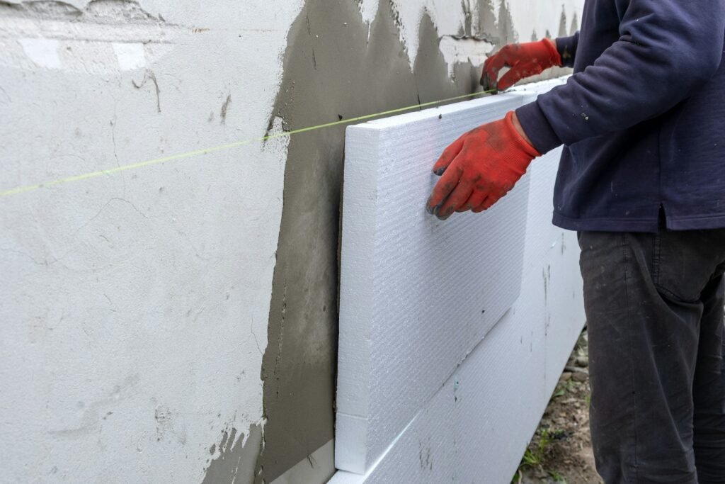 Construction worker installing styrofoam insulation sheets on house facade wall