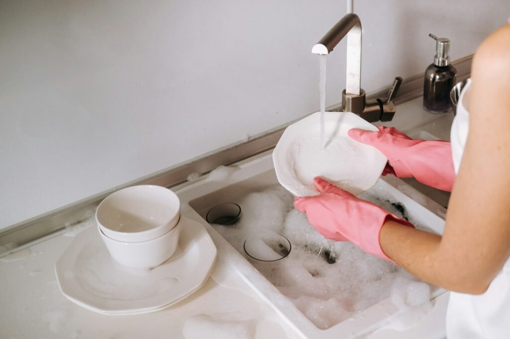 housewife girl in pink gloves washes dishes by hand in the sink with detergent. The girl cleans the