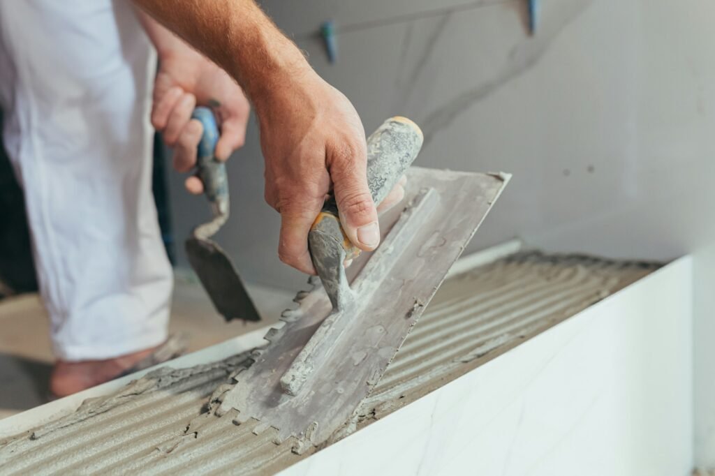 Male worker professional mounts ceramic tile in bathroom photo with close spatula with glue