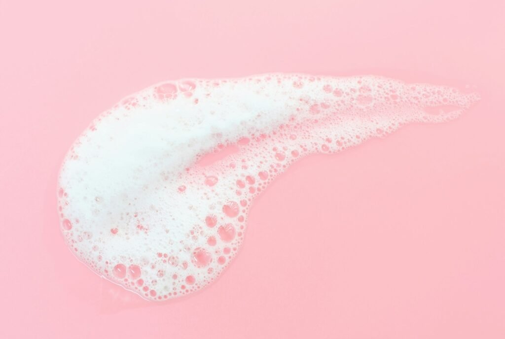 Smear of cleansing facial foam close-up on a pink background top view.