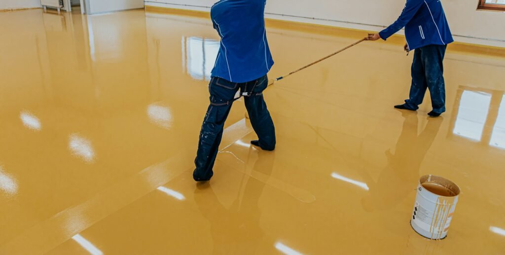 Worker, coating floor with self-leveling epoxy resin in industrial workshop.