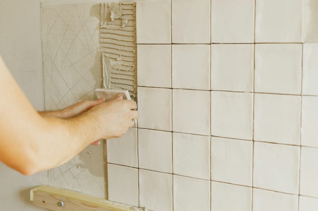 Worker installing stylish white tiles on plaster wall in sunlight