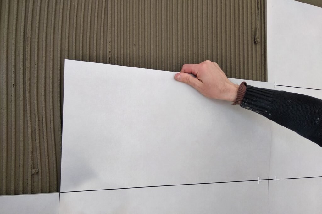 Arbeiderhender som setter keramiske fliser på veggen.