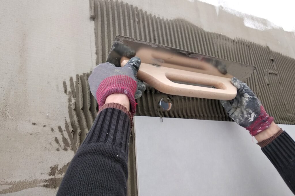 Arbeiderhender som setter keramiske fliser på veggen.